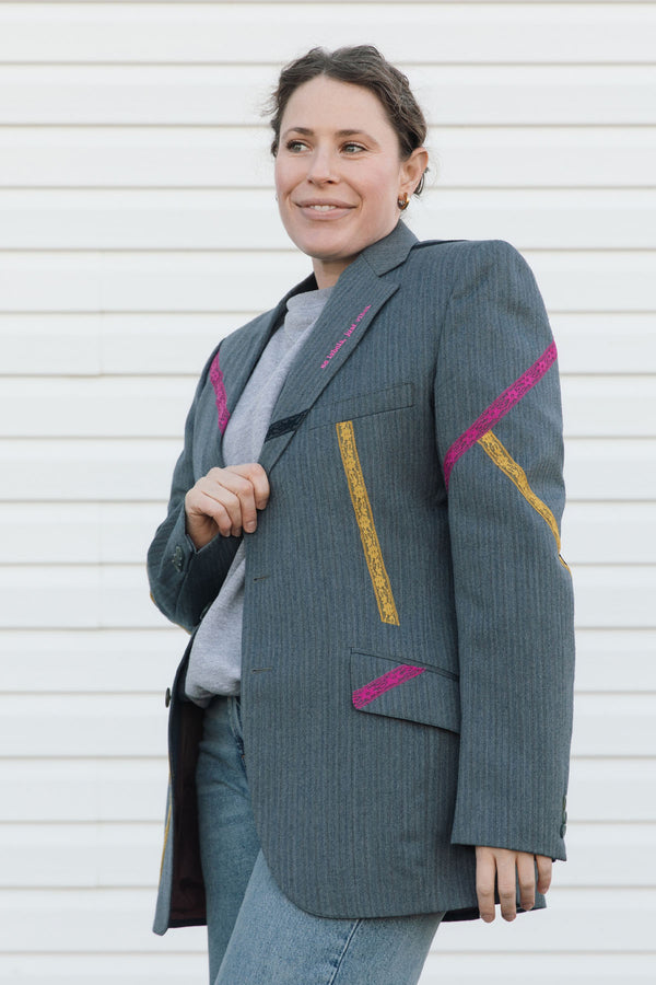 Woman wearing a gray blazer with pink and yellow accents against a white background