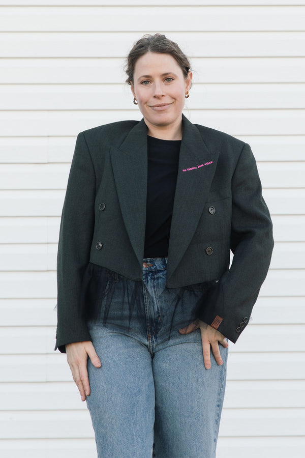 Person wearing a black blazer over a black top and blue jeans against a white background