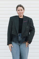 Person wearing a black blazer over a black top and blue jeans against a white background