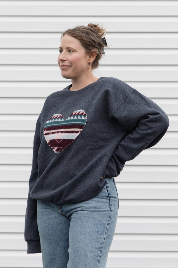 Woman wearing a dark gray sweatshirt with a colorful heart design sewn in canada
