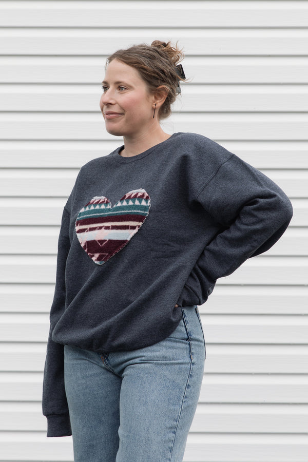 Woman wearing a dark gray sweatshirt with a colorful heart design sewn in canada