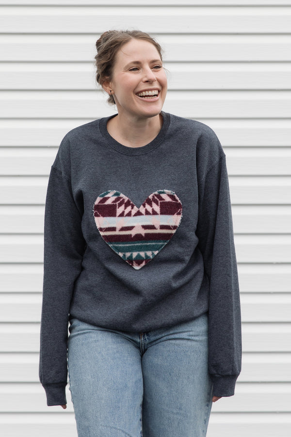 Woman wearing a dark gray sweatshirt with a colorful heart design sewn in canada