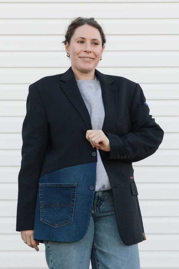 Person wearing a black blazer over a denim shirt with a white background