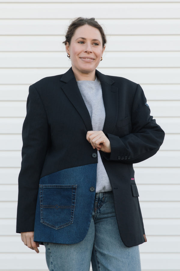 Person wearing a black blazer over a denim shirt with a white background