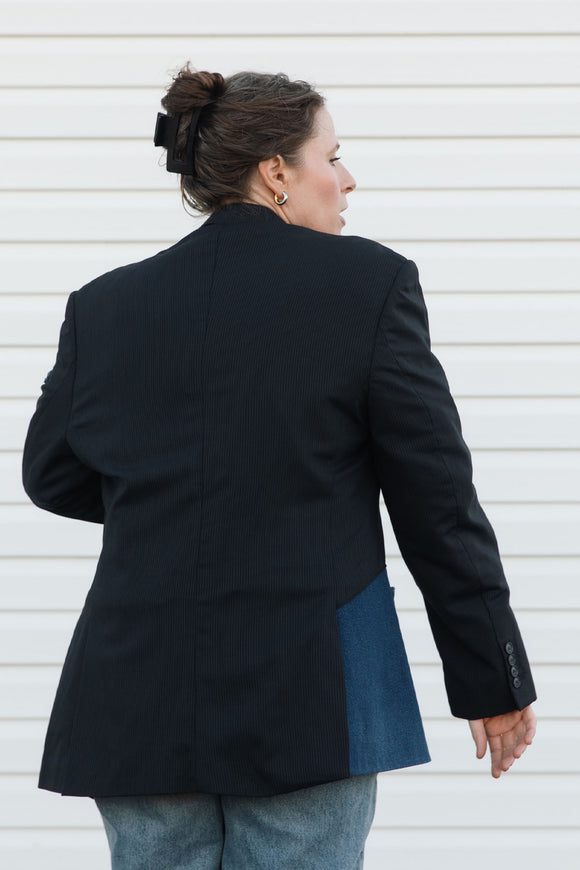 Person wearing a black blazer and light blue jeans against a white background