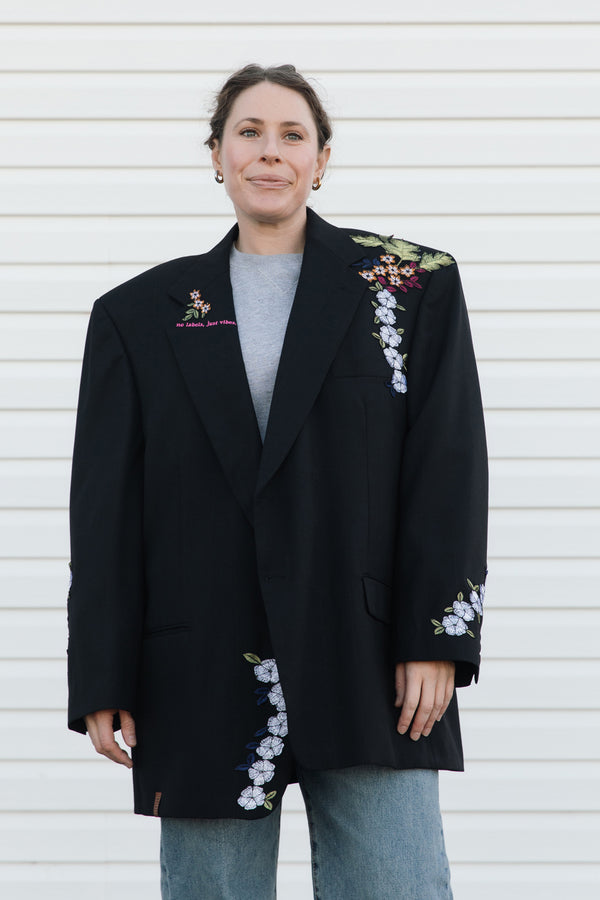 Person wearing a black blazer with floral embroidery against a white background