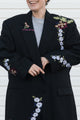 Person wearing a black coat with floral embroidery on a white background