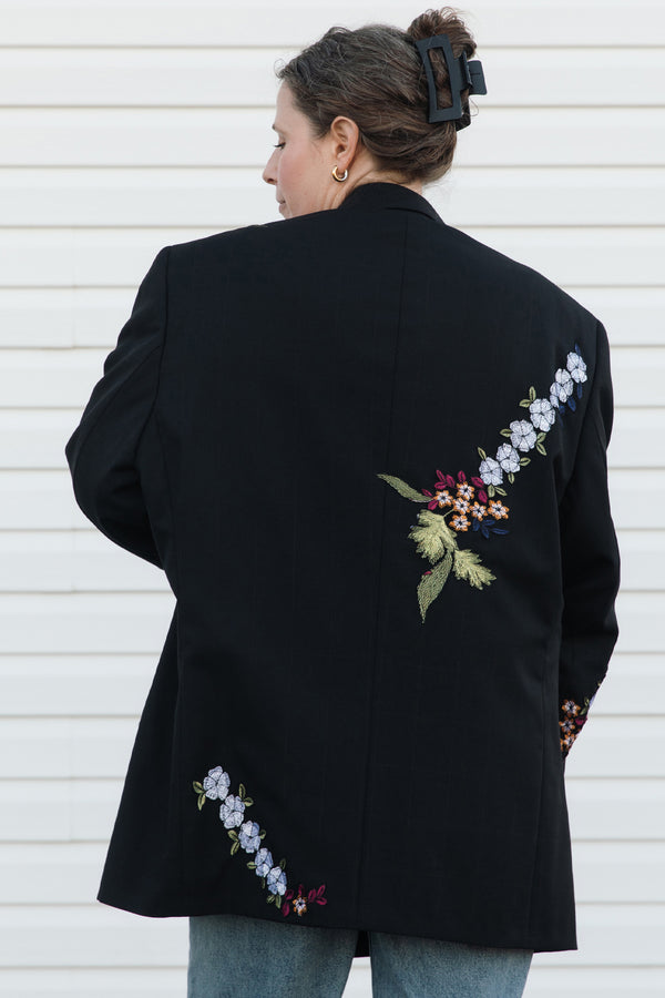 Person wearing a black blazer with floral embroidery on the back against a white background