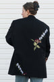 Person wearing a black blazer with floral embroidery on the back against a white background