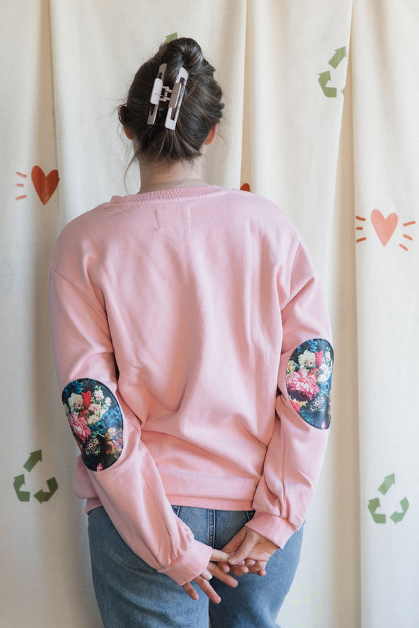 Person wearing a pink sweatshirt with 'no labels, just vibes.' embroidered on front, 100% cotton, featuring floral faux leather elbow patches upcycled in canada