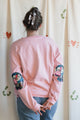 Person wearing a pink sweatshirt with 'no labels, just vibes.' embroidered on front, 100% cotton, featuring floral faux leather elbow patches upcycled in canada