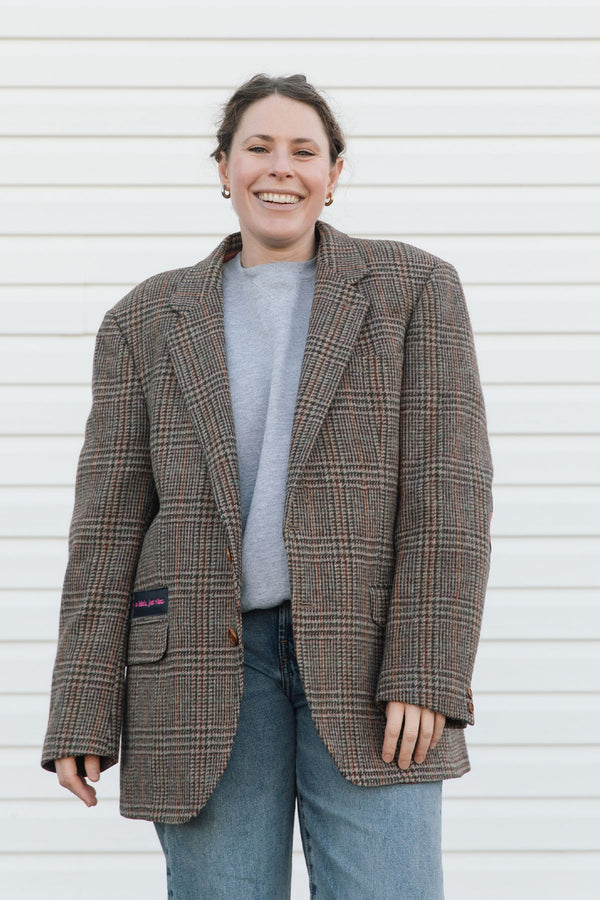 Person wearing a plaid blazer over a gray shirt and blue jeans against a white background