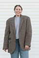Person wearing a plaid blazer over a gray shirt and blue jeans against a white background