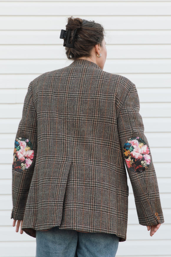 Person wearing a plaid blazer with floral embroidery on sleeves against a white background