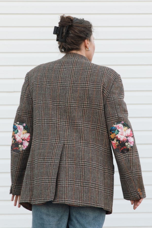 Person wearing a plaid blazer with floral embroidery on sleeves against a white background