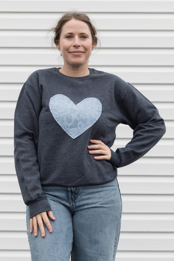 Woman wearing a denim floral heart on a charcoal sweater sewn in canada