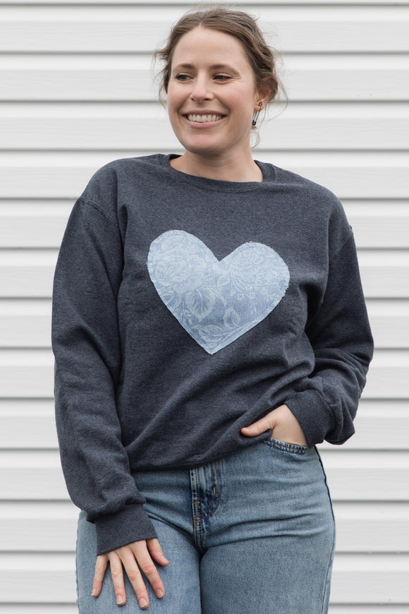 Woman wearing a denim floral heart on a charcoal sweater sewn in canada