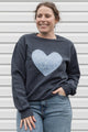 Woman wearing a denim floral heart on a charcoal sweater sewn in canada
