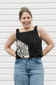 Woman wearing a black tank top with a white floral design and blue jeans standing against a white background, black linen tank top, upcycled in canada