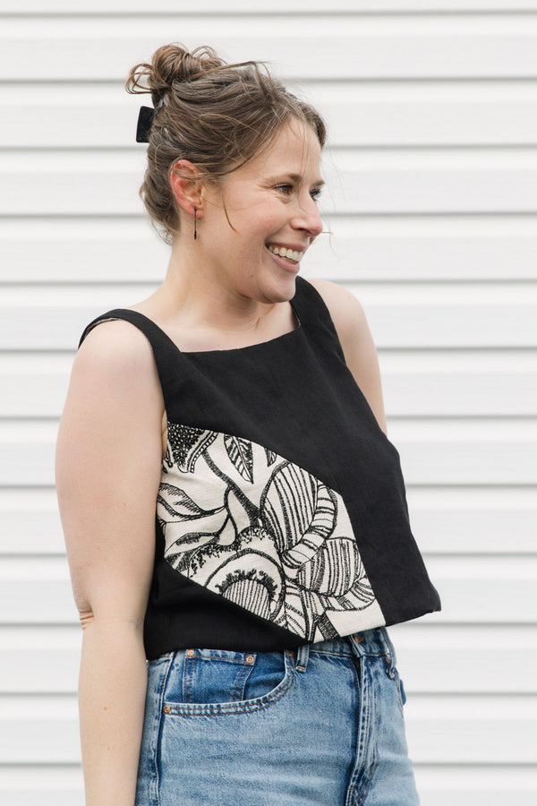 Woman wearing a black tank top with a white floral design and blue jeans standing against a white background, black linen tank top, upcycled in canada