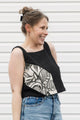 Woman wearing a black tank top with a white floral design and blue jeans standing against a white background, black linen tank top, upcycled in canada