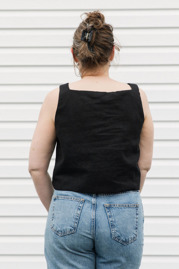 Woman wearing a black tank top with a white floral design and blue jeans standing against a white background, black linen tank top, upcycled in canada