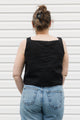 Woman wearing a black tank top with a white floral design and blue jeans standing against a white background, black linen tank top, upcycled in canada