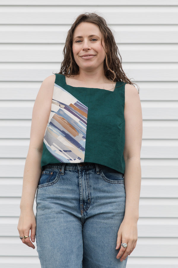 Woman wearing a sleeveless top with a geometric pattern and blue jeans against a white background