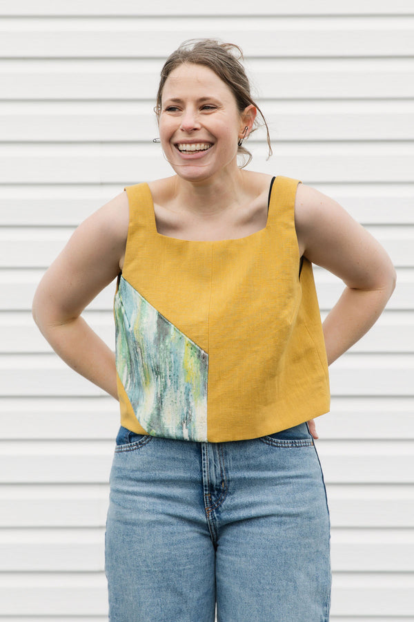 Woman wearing a mustard yellow tank top with a colorful design on a white background