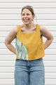 Woman wearing a mustard yellow tank top with a colorful design on a white background