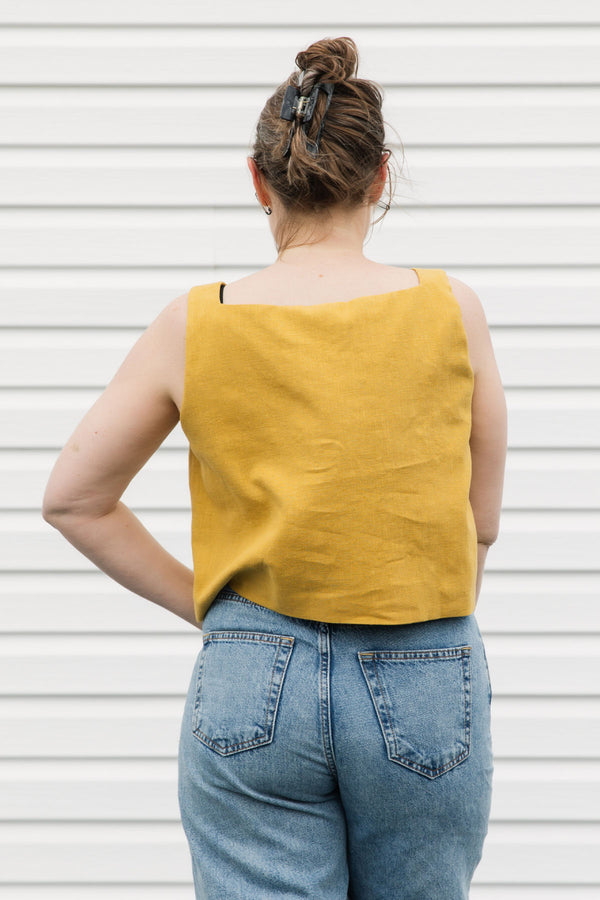 Person wearing a yellow sleeveless top and blue jeans against a white background