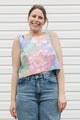 Woman wearing a floral sleeveless top and jeans standing against a white wall.