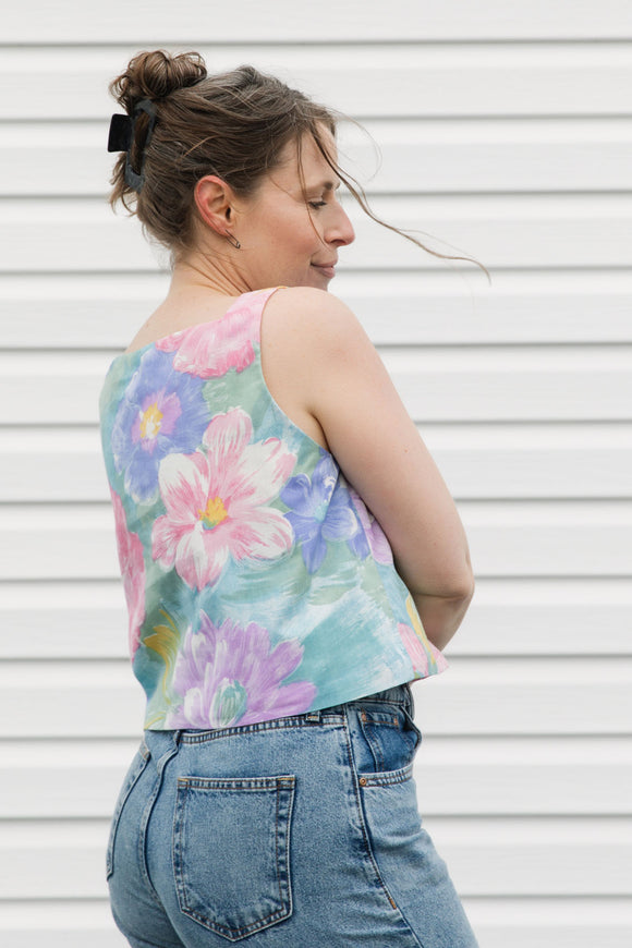 Woman wearing a colorful floral sleeveless top and blue jeans against a white background