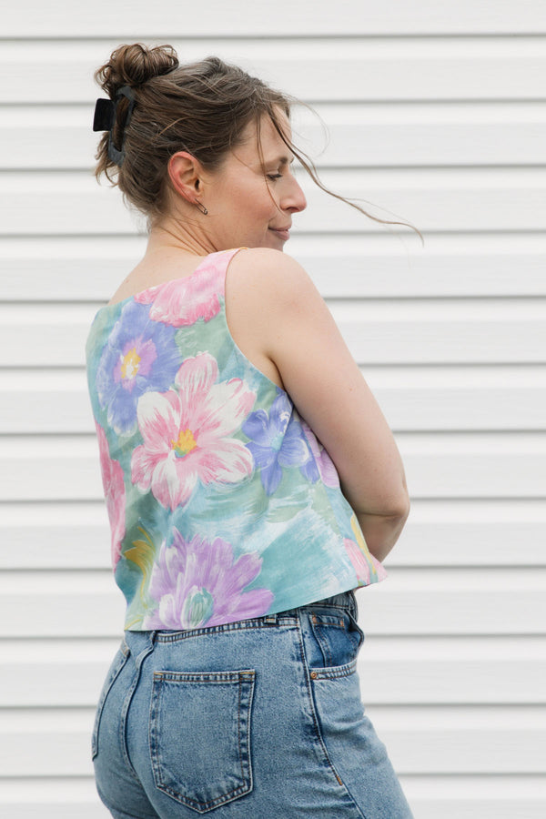 Woman wearing a colorful floral sleeveless top and blue jeans against a white background