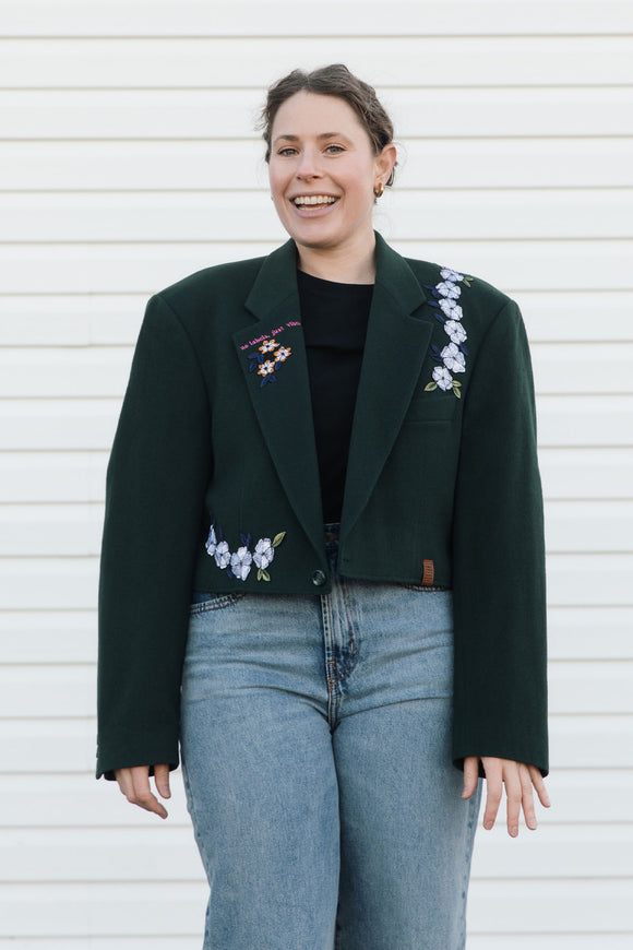 Woman wearing a dark green blazer with floral embroidery against a white background