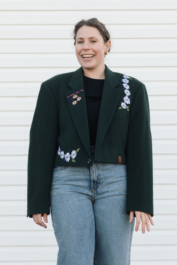 Woman wearing a dark green blazer with floral embroidery against a white background