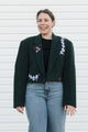 Woman wearing a dark green blazer with floral embroidery against a white background