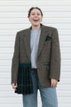 Person wearing a plaid blazer over a tartan skirt against a white background