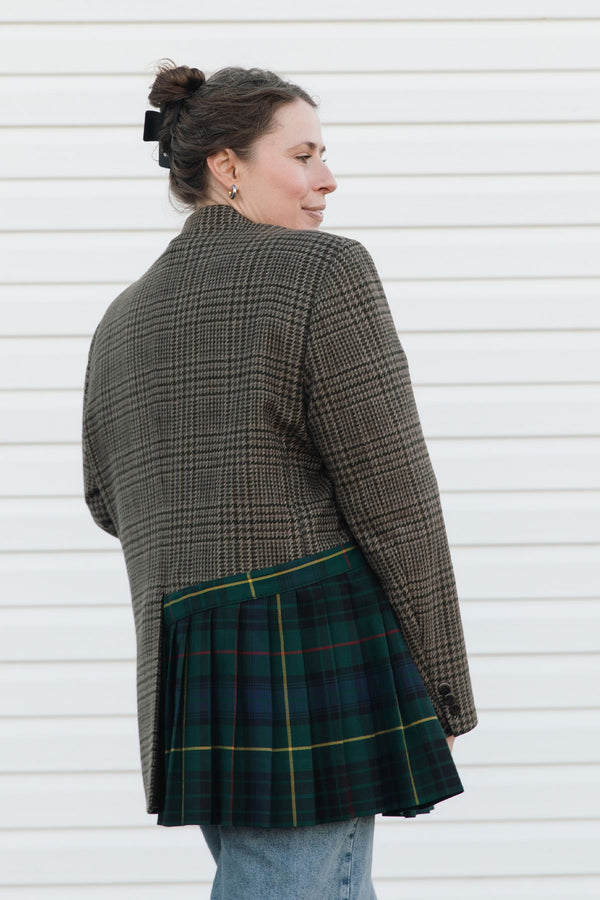 Person wearing a plaid jacket and green tartan skirt against a white background