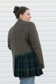 Person wearing a plaid jacket and green tartan skirt against a white background