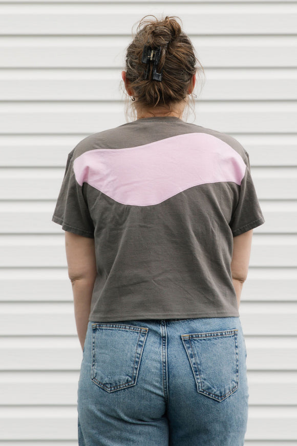 Person wearing a gray t-shirt with a pink design on the back against a white wall.