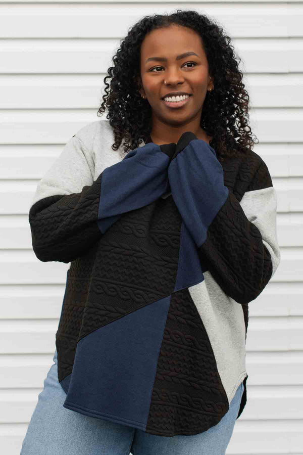 person wearing a patchwork sweater, upcycled from scrap fabric, grey, black and navy colours. comfy oversized fit made in Canada