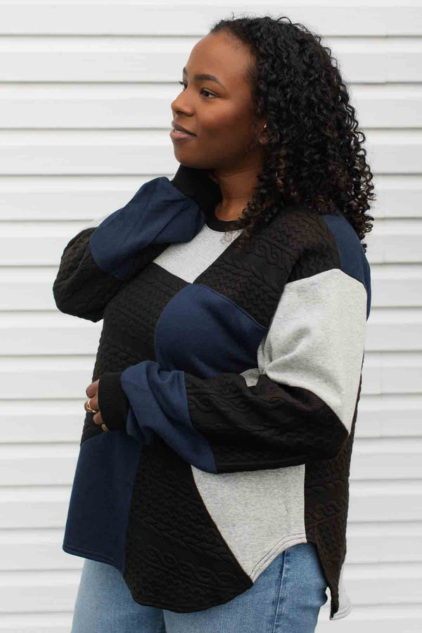 person wearing a patchwork sweater, upcycled from scrap fabric, grey, black and navy colours. comfy oversized fit made in Canada
