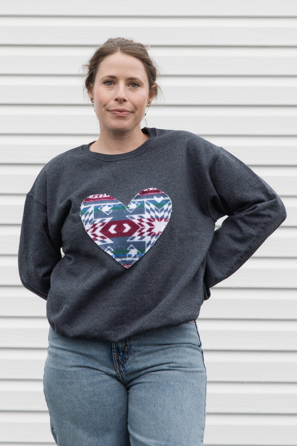 Person wearing a dark gray sweatshirt with a colorful heart design sewn in canada