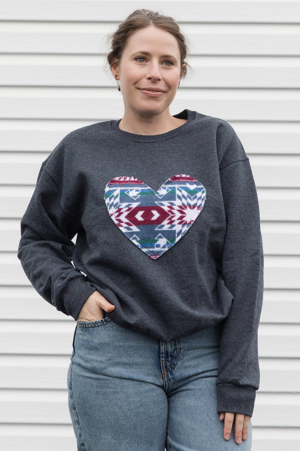 Person wearing a dark gray sweatshirt with a colorful heart design sewn in canada