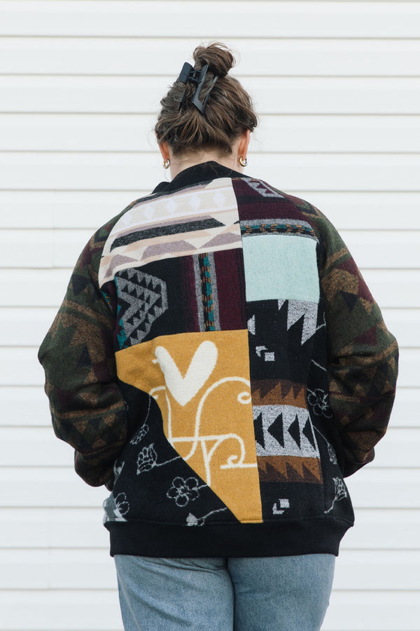 Person wearing a colorful patchwork jacket with geometric patterns against a white background