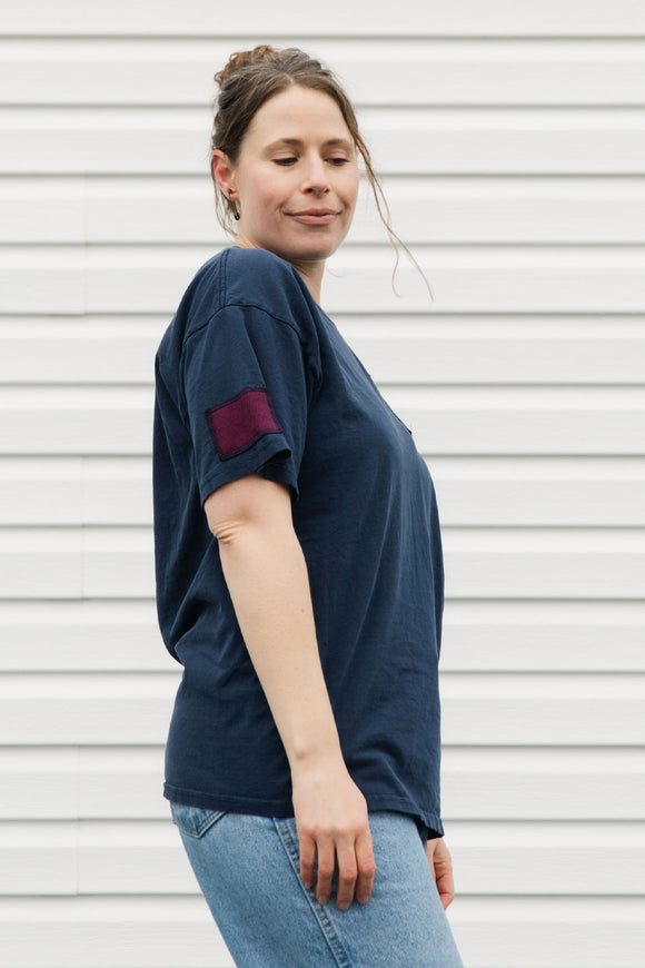 Woman wearing a navy blue t-shirt with a red sleeve patch against a white background