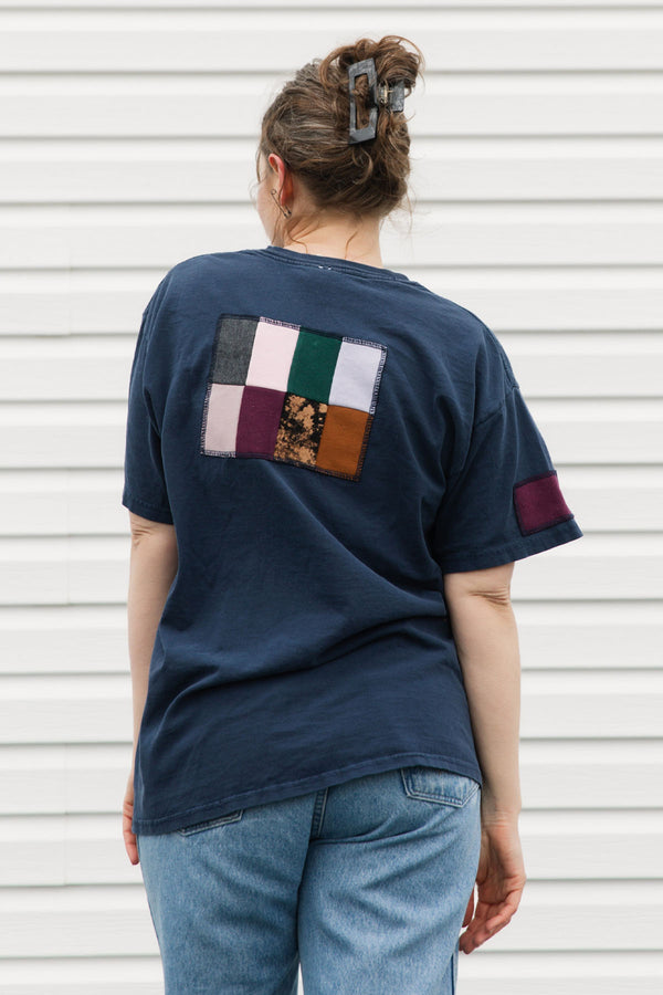 Person wearing a navy blue t-shirt with a colorful patch on the back against a white background