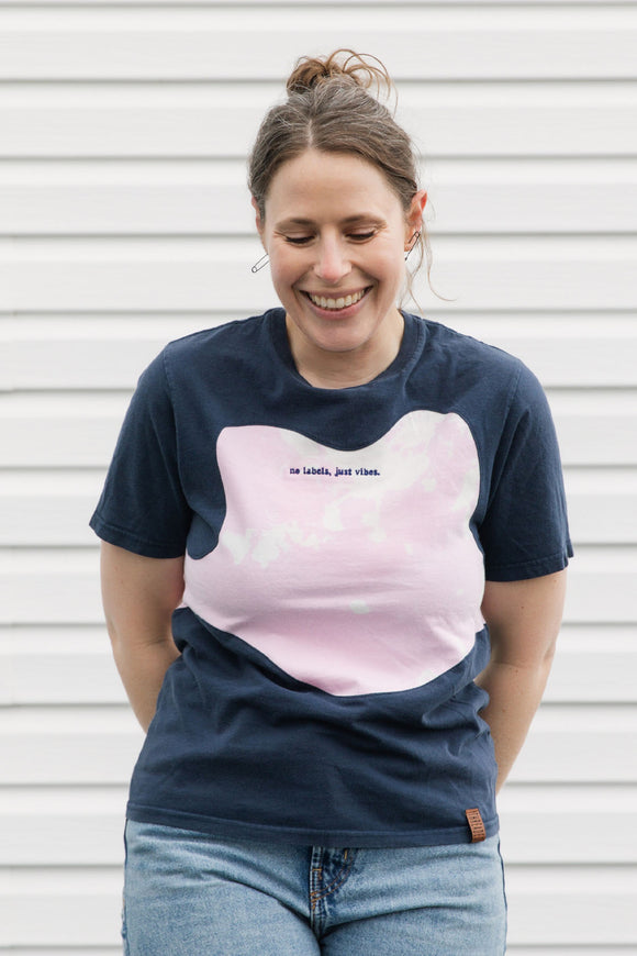 Woman wearing a navy blue and pink t-shirt with text, standing against a white wall.