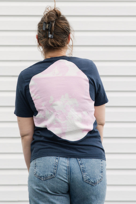 Person wearing a navy and pink tie-dye t-shirt with blue jeans against a white background